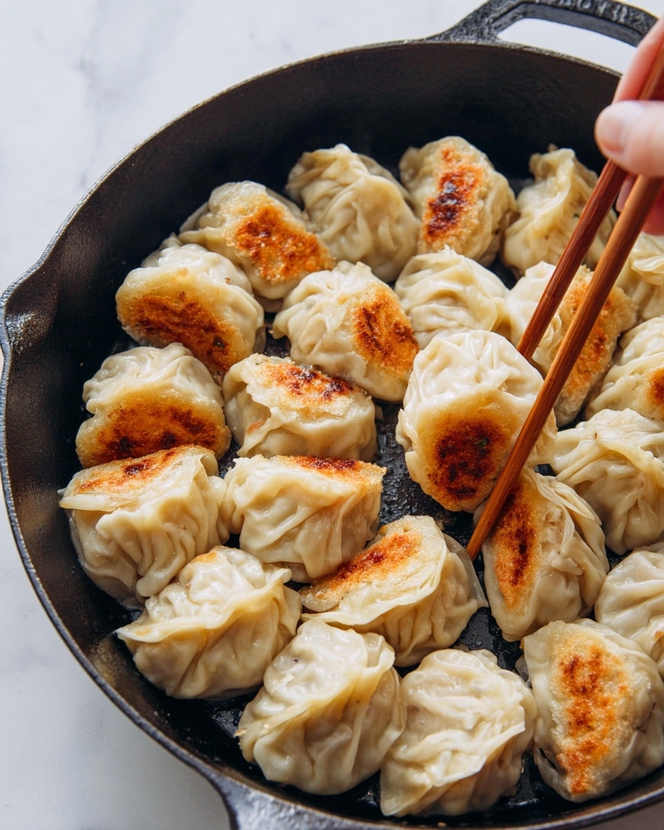 The image shows a white oval plate with twelve pan-fried dumplings arranged in a loose circle. Each dumpling has a light beige dough with a soft, slightly translucent texture, and a golden-brown crispy patch on one side. The dumplings vary in shape, some with a simple crescent fold, others with pleated edges, giving a mix of smooth and ridged surfaces. Next to the plate, there are two light brown wooden chopsticks resting on the white marbled surface. To the top left, a small white bowl with a colorful blue and red pattern around the rim holds a dark red chili oil sauce with visible chili flakes. Green scallion stalks lie diagonally next to a white cloth napkin beside the bowl. Part of a red and white ceramic teapot with intricate patterns is visible at the top right corner. Photo taken with an iphone --ar 4:5 --v 7